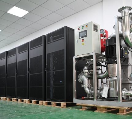 Whatsminer Hydro Cooling Cabinet (2 numbers), showcasing a row of tall black server cabinets designed for cryptocurrency mining operations, with a large metallic cooling system equipped with pipes and pumps to the right, all placed on wooden pallets in an industrial setting